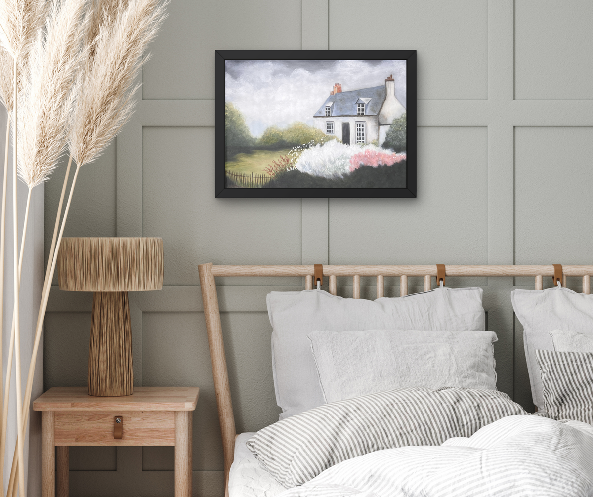 A framed landscape painting of a cottage in a field hangs on a gray paneled wall above a bed with white and gray striped bedding in a styled bedroom setting.