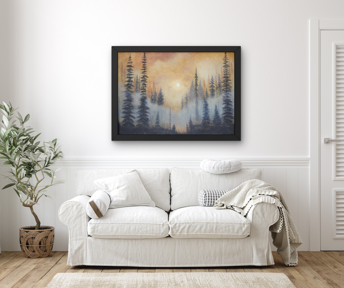 A framed landscape art print depicting a misty pine forest at sunset, displayed on a white wall above a white sofa in a styled living room.