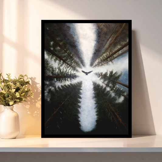 A framed vertical art print leaning against a wall on a shelf, showing an upward view of tall dark trees with a bright white light or bird at the center. A white vase with greenery sits beside it on the shelf.