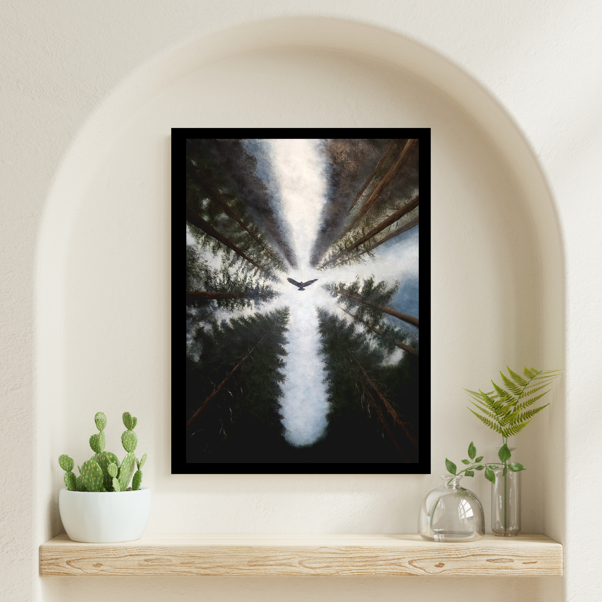 A framed vertical art print featuring a forest scene with a bird silhouette against a bright sky, displayed on a wooden shelf inside a cream-colored arched wall niche with small potted plants.