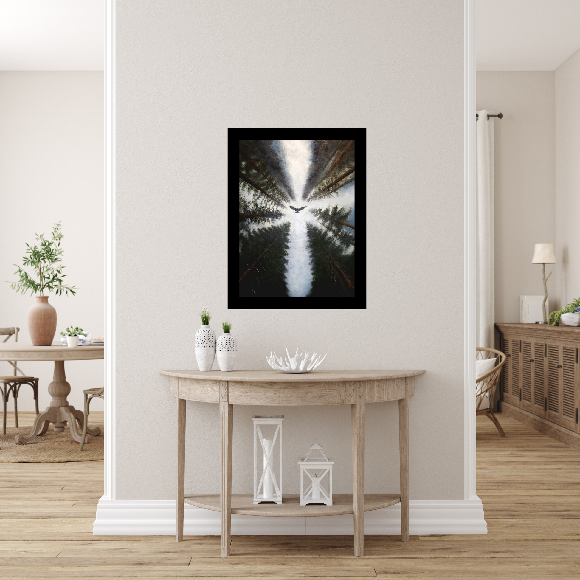 A framed black and white forest landscape print hangs on a beige wall above a light wood console table in a modern, bright entryway.